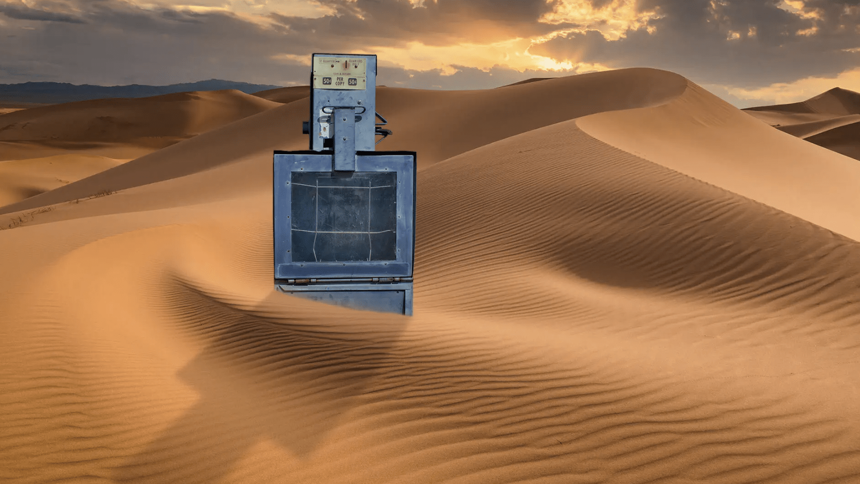 Photo of an newspaper stand on top of sand dunes.