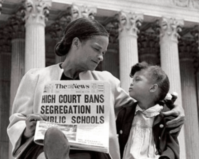 Vintage photo showing a women with a child holding a newspaper with the headline: High Court Bans Segregation in Public Schools.